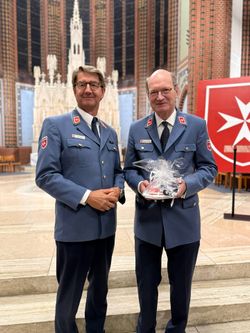 Herr Kramer und Herr Stolberg stehen vor dem Altar und lächeln in die Kamera. Herr Stolberg hält ein Geschenk in der Hand.