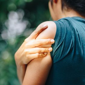 Eine Person fasst sich mit der Hand an den Oberarm.