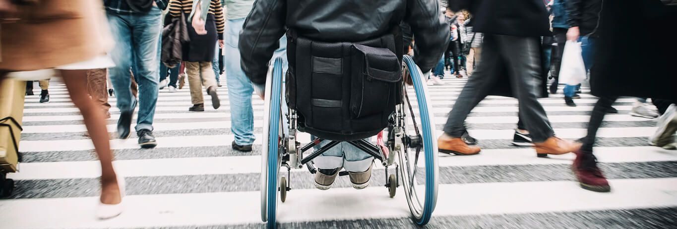Ein Rollstuhlfahrer in einer Menschenmenge auf einem Zebrastreifen.