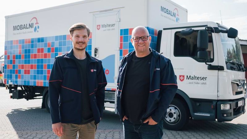 Zwei lächelnde Männer stehen vor einem Lkw 