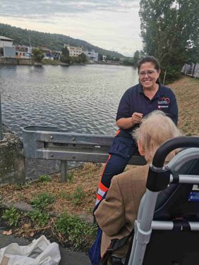 Der Gast und eine Malteser Helferin sitzen vor einem See und Blicken sich an 
