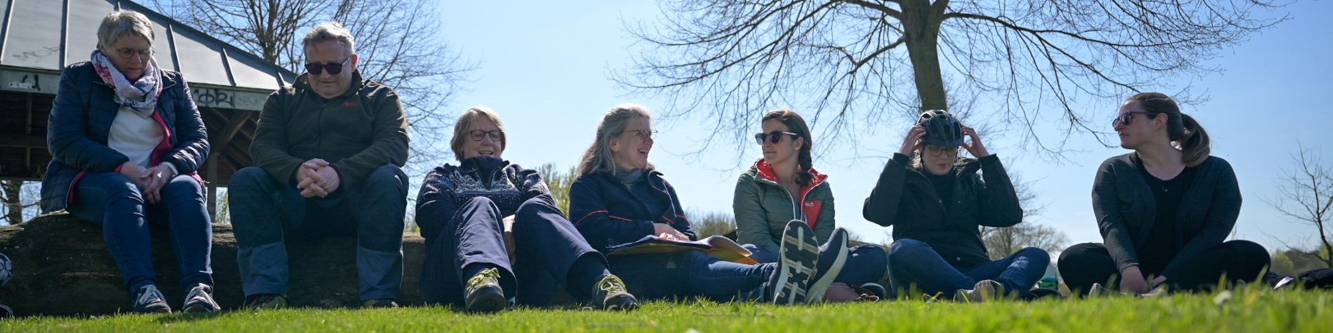 Dörte Schrömges sitzt mit einer Gruppe auf einer Wiese und unterhält sich. Sie machen Pause von ihrer Fahrrad-Tour.
