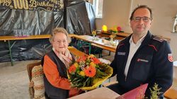 Die Jubilarin sitzt mit einem Blumenstrauß in der Hand an einem Tisch, daneben sitzt Malteser Kreisgeschäftsführer Roland Bucher