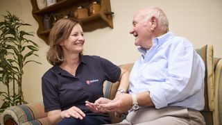 Eine lächelnde Frau und ein älterer Mann sitzen auf einem Sofa und unterhalten sich.