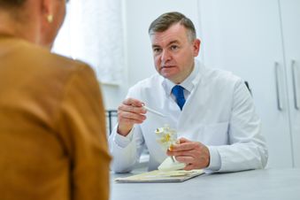 Ärztliche Fachkraft erklärt einer Patientin mithilfe eines Wirbelsäulenmodells die Diagnose im Sprechzimmer.