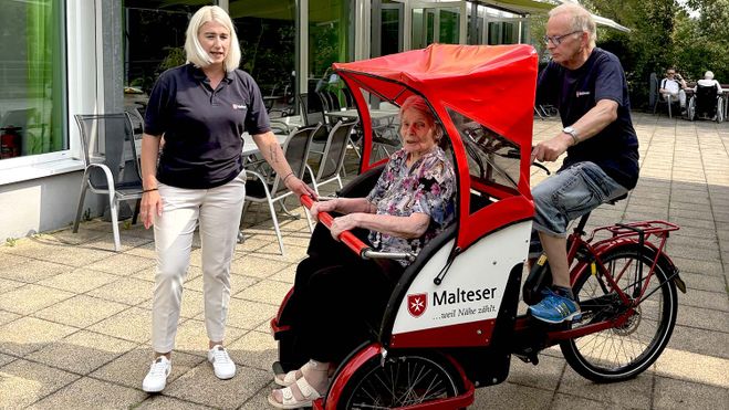 Eine Frau sitzt in einer Fahrradrikscha der Malteser. 