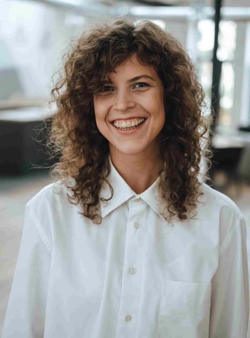 Porträtaufnahme einer jungen, lächelnden Frau in einem weißen Hemd. 