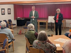 Eine weitere freiwillige Ehrenamtliche der Malteser steht rechts neben Jan Phillip Lehmker und soll sich ein Wort ausdenken und uneinsehbar aufschreiben.