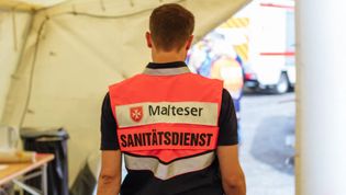 Malteser Sanitäter im Zelt von hinten fotografiert.