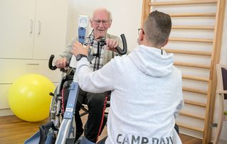 Ein älterer Herr mit Pfleger beim Training auf einem Fahrrad