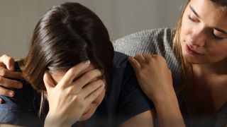 Eine Frau legt einer anderen Frau die Arme um die Schulter und tröstet sie in ihrer Trauer. 