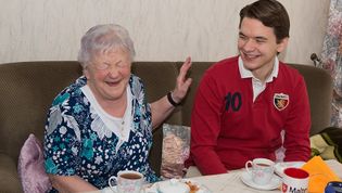 Seniorin lacht herzhaft auf dem Sofa.