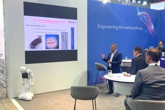 Mann bei Präsentation auf Fachmesse, medizinische Inhalte auf Leinwand, Roboter vorne links, Publikum an Tischen.