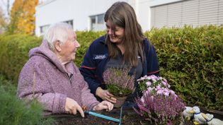 Ältere Frau arbeitet mit Malteser Helferin im Garten