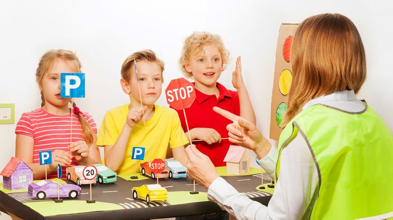 Kinder mit gebastelten Verkehrsschildern in den Händen vor einem Straßenmodell aus Papier