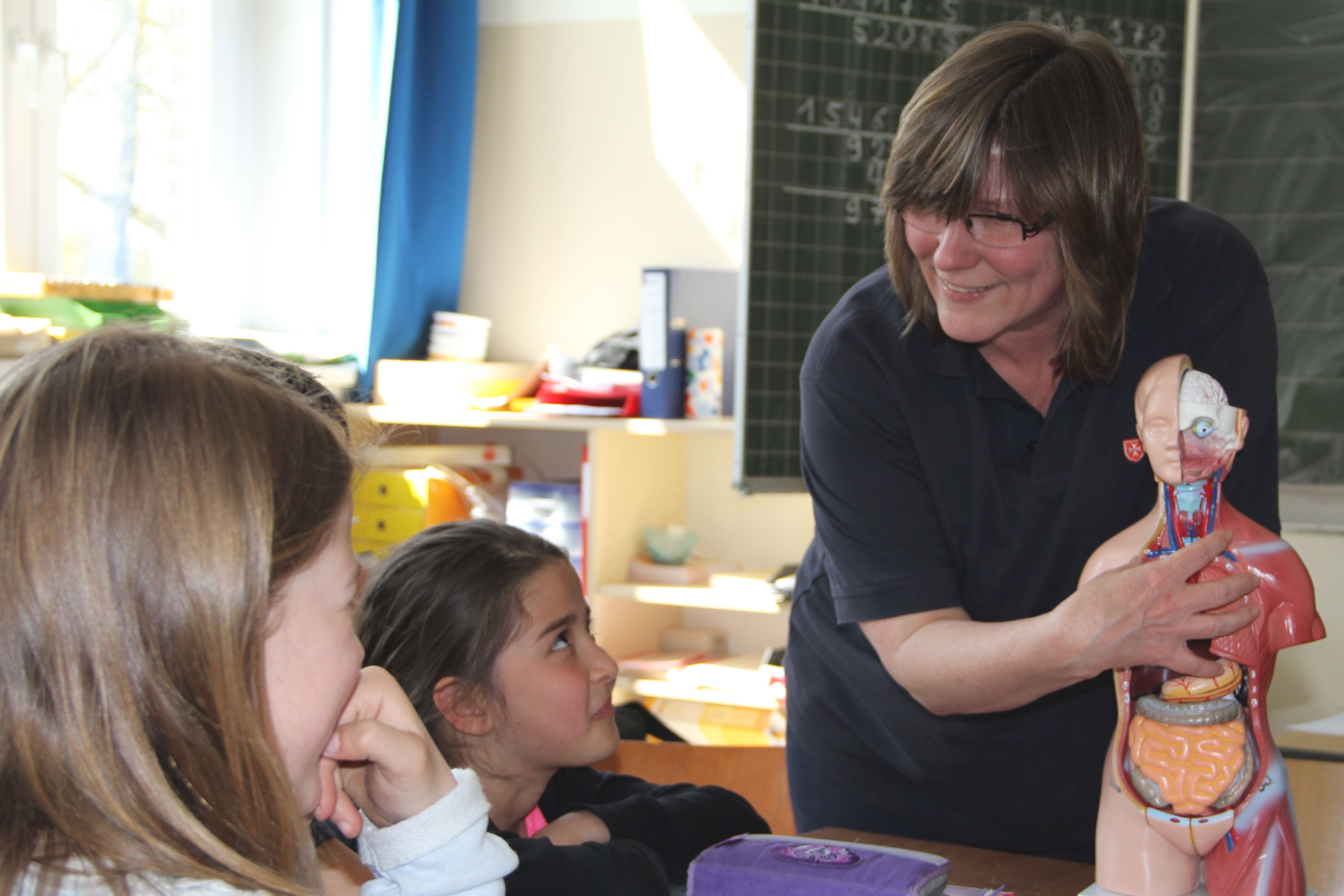 Eine Mitarbeiterin der Malteser zeigt Kindern in einer Schule den anatomischen Aufbau eines Menschen anhand eines Modells.