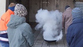 Ein Mann löscht ein Feuer in einer Feuerschale, während ein Malteser Ausbilder und weitere Kursteilnehmende zuschauen.