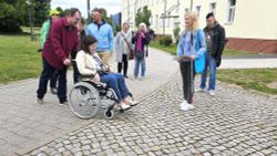 Annemarie Kock sitzt im Rollstuhl. Mehrere Menschen begleiten ihre Test-Aktion.