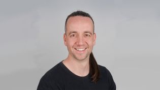 Porträt einer Person mit langem Haar vor neutralem, hellem Hintergrund.