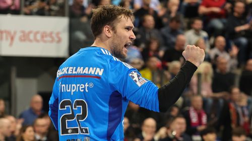 Handballtorwart mit dem Rücken zur Kamera hebt die jubelnd Faust während eines Spiels.