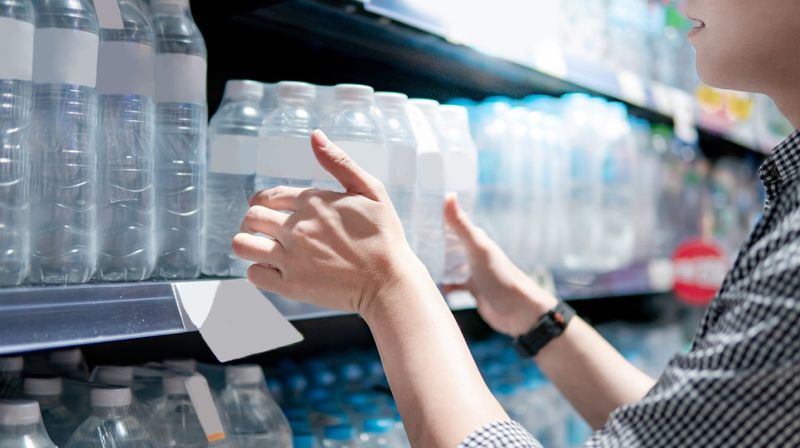 Eine junge Frau nimmt ein Sechserpack Wasser aus einem Supermarktregal