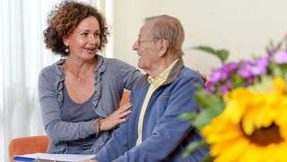 Eine Frau unterhält sich mit einem älteren Mann und legt ihm den Arm um die Schultern.