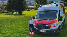 Eine junge Frau in Einsatzkleidung steht vor einem Krankentransportwagen.