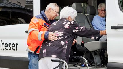 Ein Helfer der Malteser hilft einer Frau beim Einsteigen in ein Fahrzeug