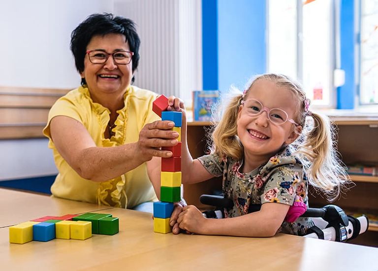Eine Kita-Begleiterin baut mit einem Kind mit Bauklötzen. 