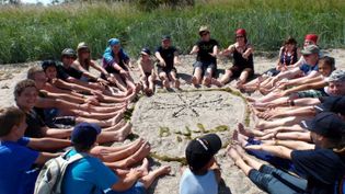 Jugendliche und Kinder der Malteser Jugend sitzen im Sand in einem Sitzkreis
