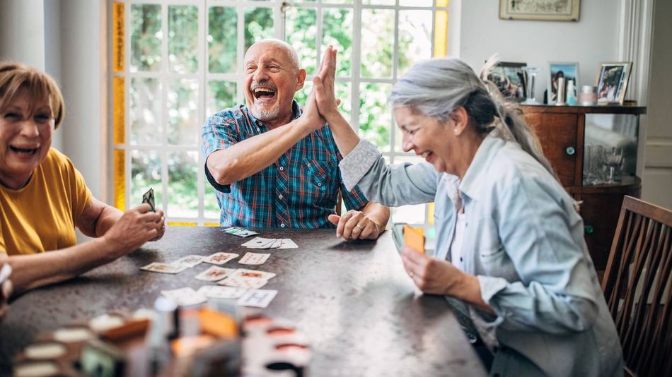 Eine Gruppe älterer Menschen spielt gemeinsam Karten, lacht dabei und klatscht sich gegenseitig in die Hände.
