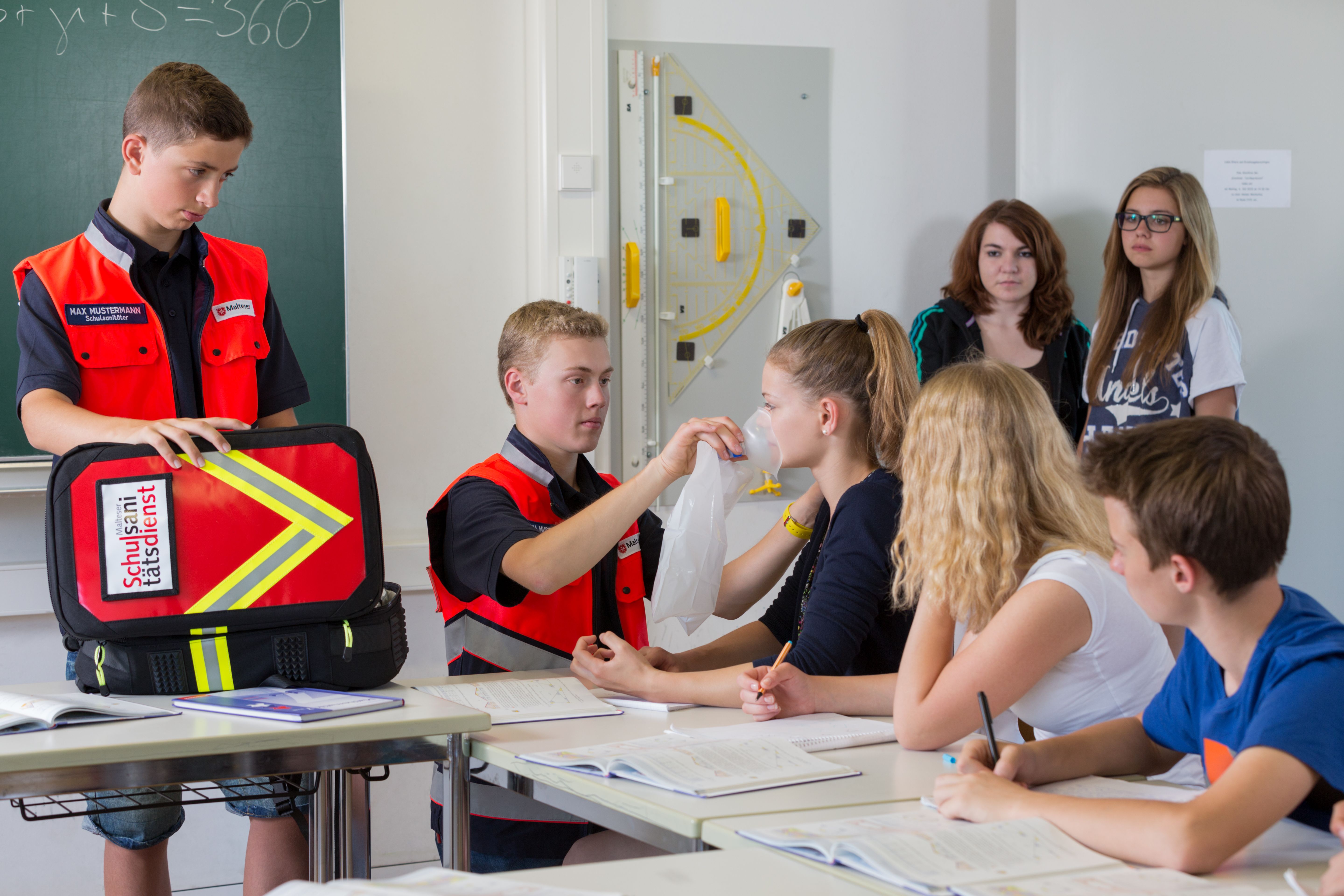 Zwei Schulsanitäter versorgen die Wunde einer Schülerin im Klassenzimmer.