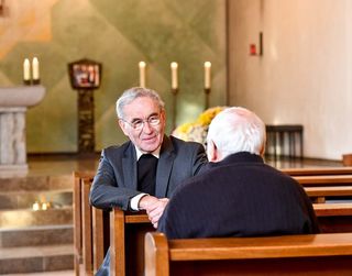 Zwei Männer sitzen gegenüber in einer Kirche und unterhalten sich