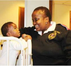 Young Siyabonga looks at a smiling staff member by his bed; original photograph from newsletter no. 35 (2016), page 8.