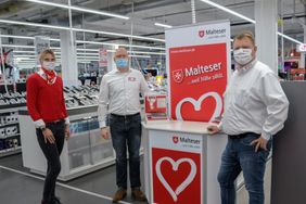 Nicole Mai-Prange (Kundendienst Hausnotruf), Sebastian (Vertriebsleiter Media Markt) und Ronny Graue (Vertriebsleiter Malteser) stehen im Media Markt vor dem Stand des Hausnotrufs.