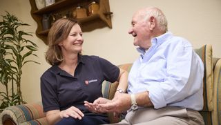 Eine lächelnde Frau und ein älterer Mann sitzen auf einem Sofa und unterhalten sich.