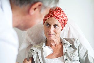 Eine in einem Krankenbett liegende Patientin im Gespräch mit einem Arzt.