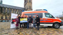 Menschen stehen mit einem großen Spendenscheck vor dem Herzenswunsch-Krankenwagen.