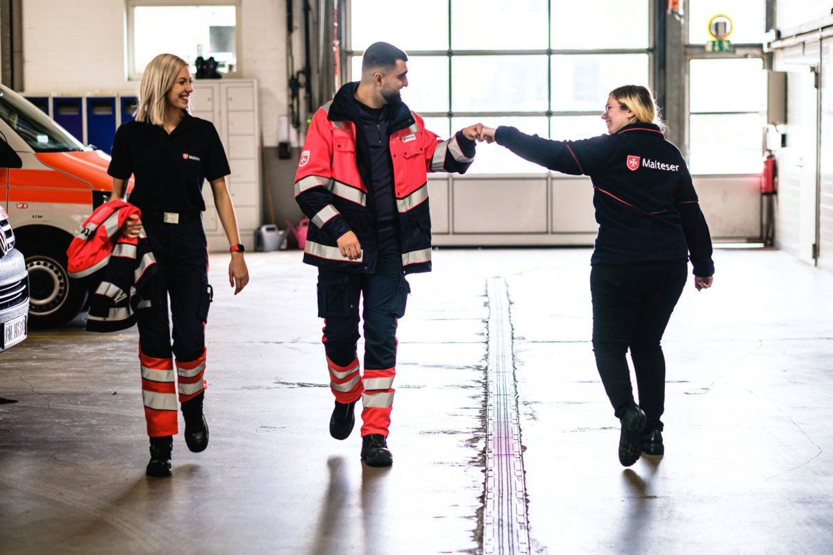 Junge, lächelnde Freiwillige der Malteser in Deutschland geben sich im Vorbeigehen einen Fistbump