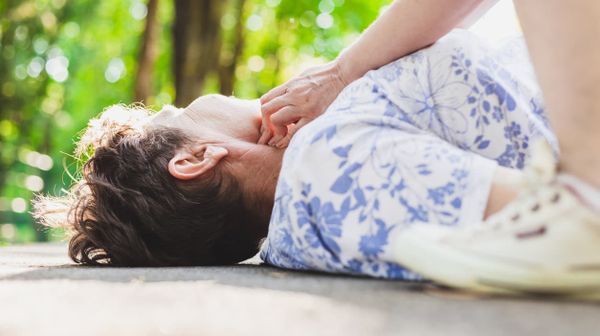 Hand einer Frau fühlt am Hals den Puls einer am Boden liegenden Seniorin.