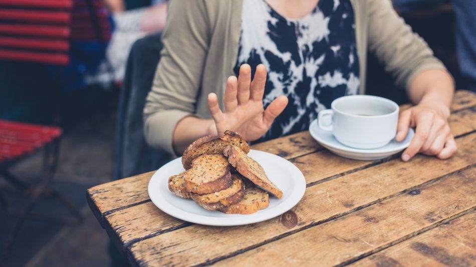 Eine ältere Frau an einem Tisch macht eine abweisende Handbewegung vor einem Teller mit Brot.