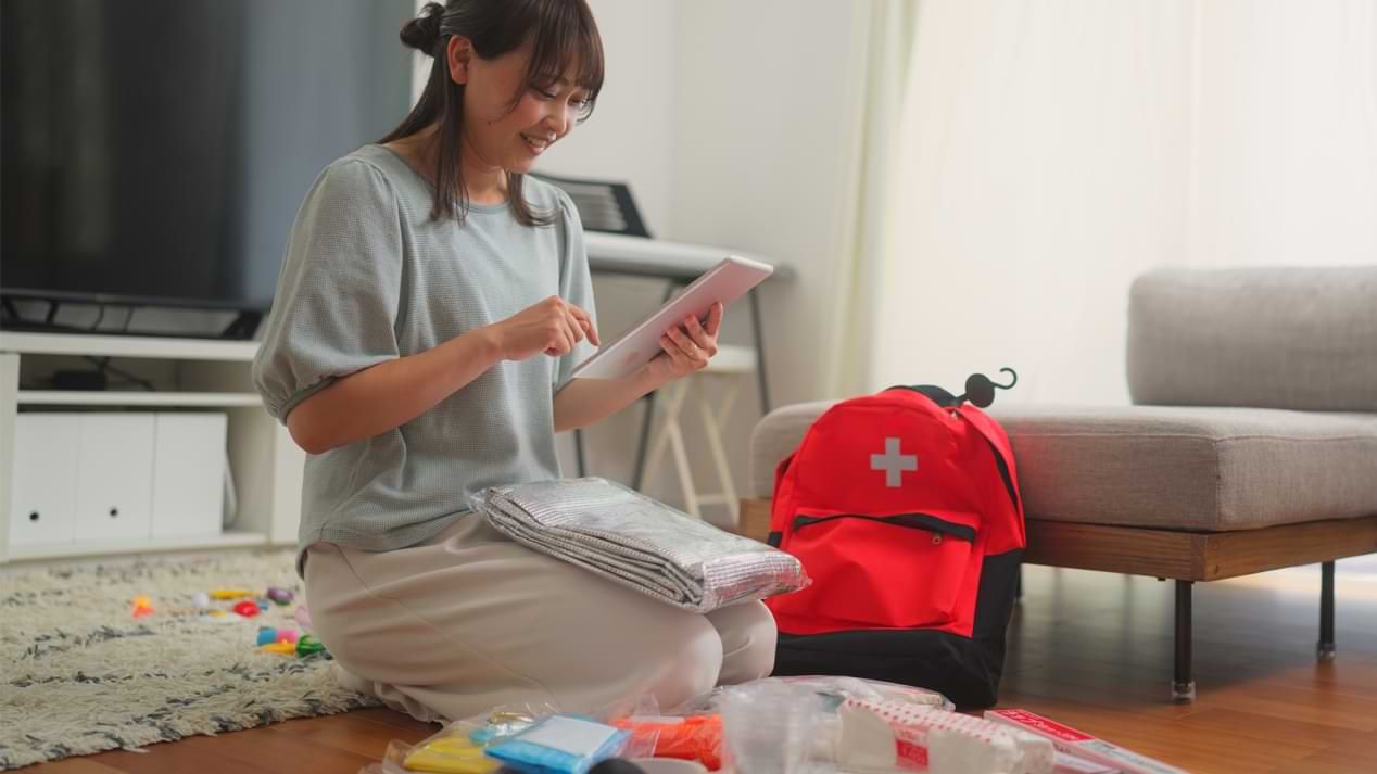 Eine lächelnde Frau packt und überprüft einen Notfall-Rucksack in ihrem Wohnzimmer.