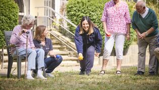 Frauen in Malteser Kleidung spielen auf einer Wiese mit Senioren ein Ballspiel