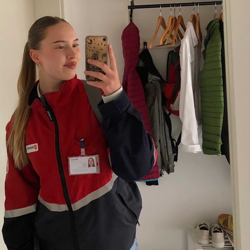 Eine junge Frau mit einer schwarz-roten Jacke macht ein Selfie vor einem Spiegel