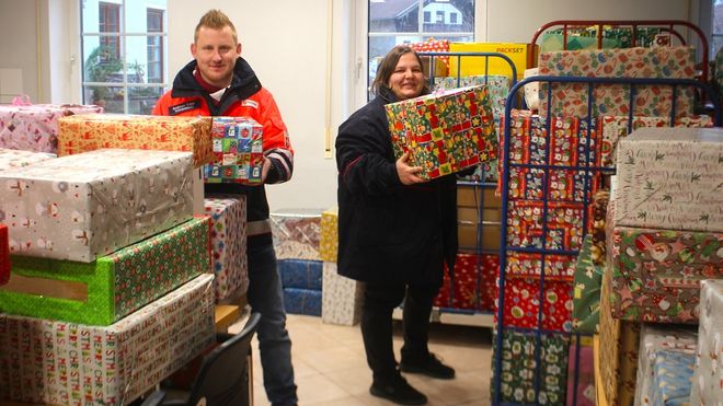 Zwei Menschen stapeln viele Pakete mit weihnachtlicher Verpackung.