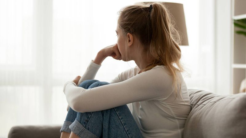 Junge Frau sitzt auf der Couch und schaut aus dem Fenster.