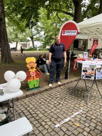 Ein Stand ist aufgebaut auf der Straße mit Informationsmaterila und Spiele für die Kinder. Im Hintergrund steht eine Malteser Mitarbeiterin.