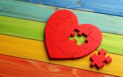Rotes Herzpuzzle mit zwei fehlenden Teilen auf einem Hintergrund mit Regenbogenfarben.
