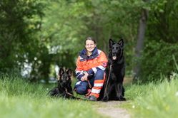 Auf dem Foto ist die Helferin Jennifer zusammen mit ihren beiden Hunden im Wald zu sehen.