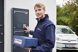 Mitarbeiter mit Warmhaltebox klingelt an einer Haustür